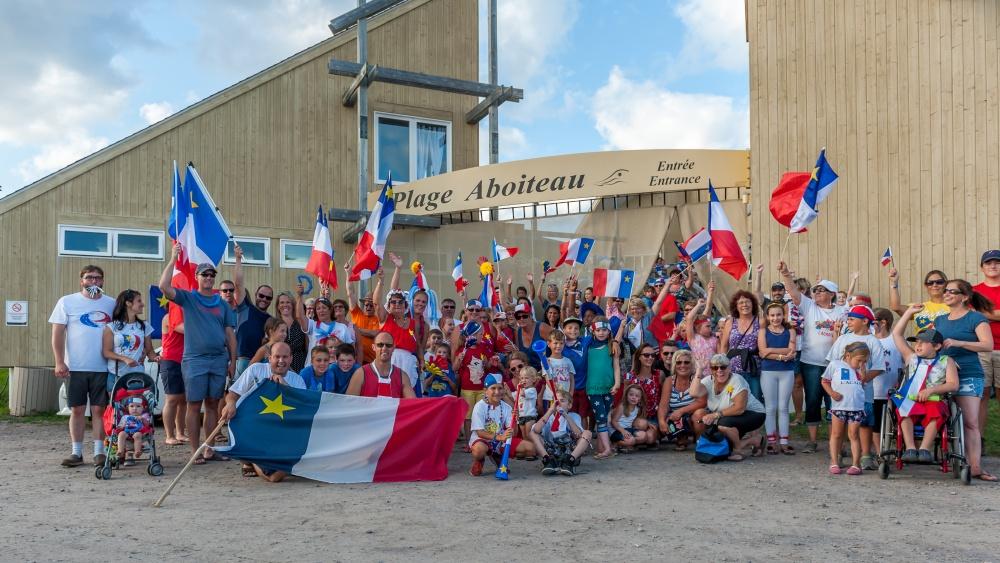 Un groupe Acadien à la Plage Aboiteau tenant des drapeaux et d'autres accessoires acadien